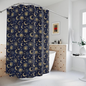 May include: A navy blue shower curtain with a repeating pattern of gold suns, crescent moons, and stars. The curtain is displayed in a bathroom with a white bathtub and a small side table.