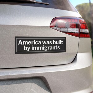 May include: A black and white bumper sticker on a silver car that reads "America was built by immigrants".