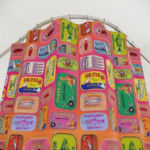 May include: A shower curtain featuring a repeating pattern of colorful sardine can labels. The labels are in various colors, including pink, green, yellow, and orange, with text in multiple languages. The curtain is suspended from a curved metal rod.