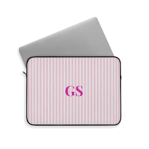 May include: A laptop sleeve with a pink and white striped pattern. The sleeve has a black border and a zipper closure. The initials "GS" are in a magenta color in the center of the sleeve. A silver laptop is partially visible.