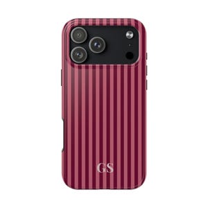 May include: A burgundy and pink striped phone case with a triple-lens camera cutout. The case has a glossy finish and the initials "GS" are at the bottom. The case is designed to fit a smartphone.