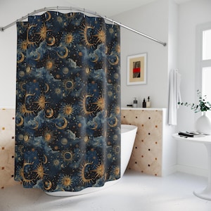 May include: A dark blue shower curtain with a celestial design featuring gold suns, moons, stars, and clouds. The curtain is hanging in a bathroom with a white bath and a small table.