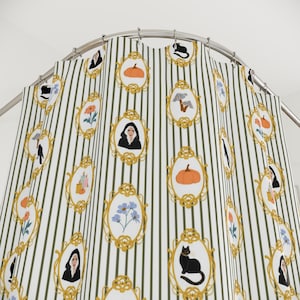May include: Shower curtain featuring a repeating pattern of framed illustrations on a striped background. The illustrations include pumpkins, cats, and portraits, framed in gold against a white and olive green striped backdrop.