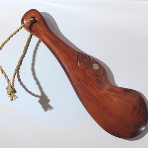 May include: A wooden carving of a stylised bird with a green stone eye. The carving is attached to a brown rope.
