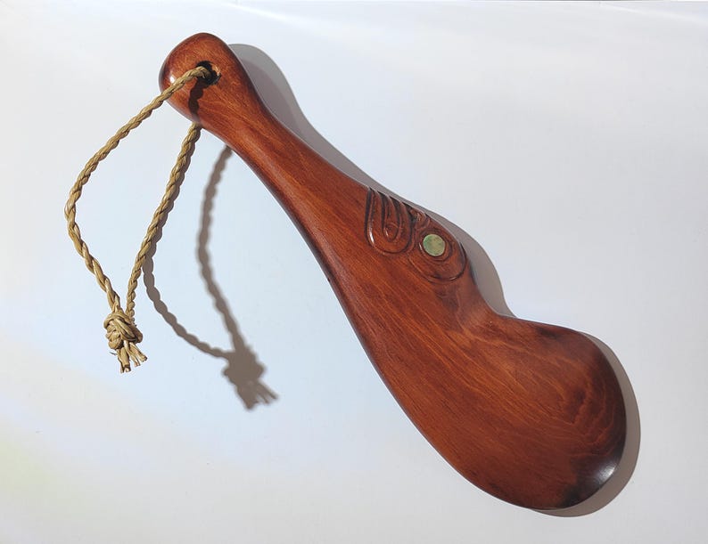May include: A wooden carving of a stylised bird with a green stone eye. The carving is attached to a brown rope.