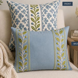 May include: A reversible square pillow featuring two distinct sides. The front displays a blue and white floral pattern with a central vertical vine motif. The back is solid blue with two vertical embroidered vine borders in green and white.