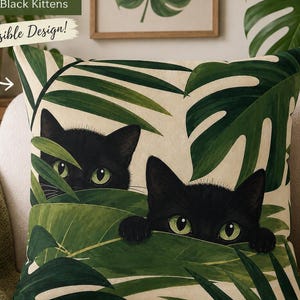 May include: A decorative pillow with a reversible design featuring black kittens peeking through green leaves. The pillow has the text "SIDE TWO Peek-a-boo Black Kittens" and "Reversible Design!"