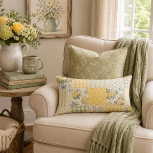 Pu&ograve; includere: Un cuscino rettangolare con un motivo patchwork di rose gialle, fiori blu e quadretti vichy gialli, posizionato su una poltrona beige con una coperta verde salvia e un cuscino verde salvia a tinta unita dietro.