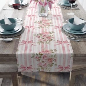 May include: A pink and white striped table runner with a floral pattern. The runner features pink roses and bows.