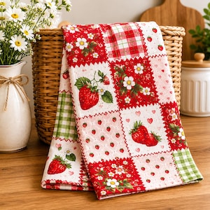 May include: A kitchen towel featuring a patchwork design of red strawberries, white flowers, and green and red gingham squares. The fabric displays various patterns including small hearts, tiny strawberries, and floral motifs on a white background.