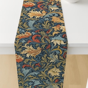 May include: A navy blue table runner with a floral pattern in shades of orange, gold, and teal. The runner is placed on a white table, with a bowl of oranges in the background. The floral design is intricate.