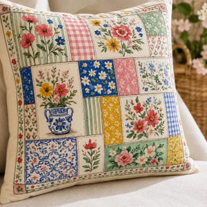 May include: Square decorative pillow with a patchwork design featuring floral patterns, gingham, and striped blocks. The pillow has a cream-colored background and a border with small floral accents. The floral arrangements include red, pink, yellow, and blue flowers.