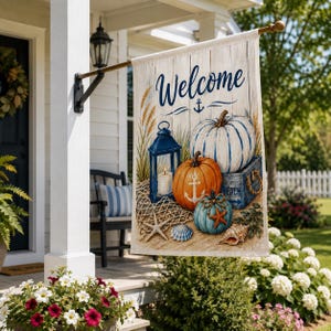 May include: A rectangular garden flag featuring the word Welcome in blue script above a nautical scene with a white pumpkin, an orange pumpkin with a white anchor, a blue pumpkin with a starfish, a blue lantern, a seashell, and a starfish.