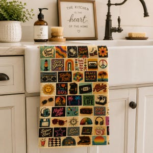 May include: A rectangular kitchen towel featuring a grid of colorful 1980s-themed illustrations, including a disco ball, cassette tape, Rubik's cube, roller skates, boombox, lava lamp, sunglasses, and various retro slogans like Good Vibes and Rad Times.