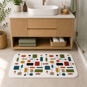 May include: White rectangular bath mat with a colorful geometric pattern. The design features squares, rectangles, and circles in teal, red, green, yellow, and black, connected by black lines. The mat is placed in front of a wooden vanity.
