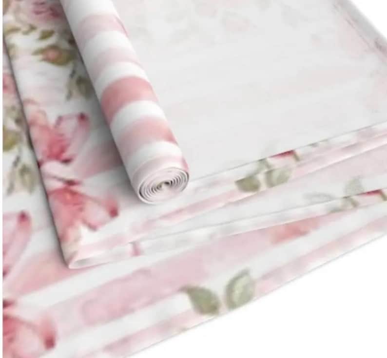 May include: Pink and white striped fabric with a floral pattern. The fabric is rolled up and the floral pattern is visible on the outside of the roll.