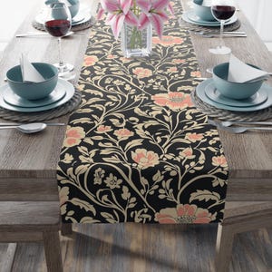 May include: A long rectangular table runner featuring a black background with a repeating floral pattern in shades of peach, cream, and light beige. The design consists of stylized flowers, winding vines, and leaves covering the entire fabric surface.