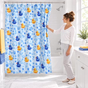 May include: A shower curtain featuring a repeating pattern of yellow rubber ducks and blue rubber ducks interspersed with light blue bubbles on a white background, suspended from a silver metal rod with rings.