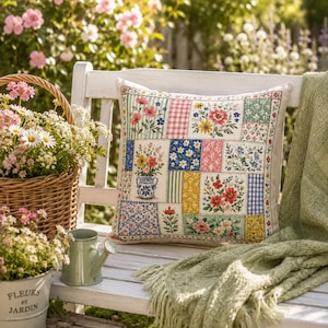 K&ouml;nnte beinhalten: Ein dekoratives quadratisches Kissen mit einem Patchwork-Design mit Blumenmustern in verschiedenen Farben. Das Kissen liegt auf einer wei&szlig;en Bank mit einer gr&uuml;nen Decke und einem Blumenkorb in der N&auml;he. Die Szene spielt sich im Freien in einem Garten ab.