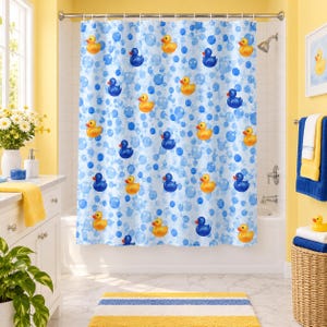May include: A white shower curtain featuring a repeating pattern of yellow and blue rubber ducks interspersed with light and dark blue circular bubbles. The curtain hangs from a silver rod with rings, covering a white bathtub in a bathroom.