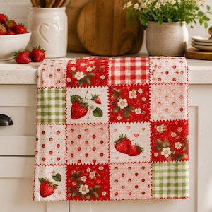 May include: A rectangular kitchen towel featuring a patchwork design of various squares. The patterns include red and white gingham, green and white gingham, and multiple prints of red strawberries, white strawberry blossoms, and small pink hearts.
