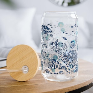 May include: A clear glass reusable water bottle with a bamboo lid and a straw. The bottle has a blue and white design of sea life, including a turtle, fish, and coral.