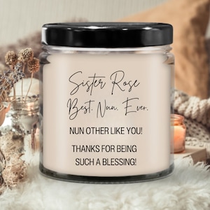 May include: A clear glass candle jar with a black lid. The candle is white and has black text that reads "Sister Rose Best. Nun. Ever. NUN OTHER LIKE YOU! THANKS FOR BEING SUCH A BLESSING!"