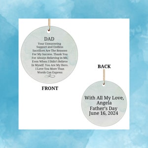 May include: A round, white ornament with a gold string. The front side has the text "DAD Your Unwavering Support and Endless Sacrifices Are The Reasons For My Success. Thank You For Always Believing in Me, Even When I Didn't Believe In Myself. You Are My Hero. I Love You More Than Words Can Express." The back side has the text "With All My Love, Angela Father's Day June 16, 2024".