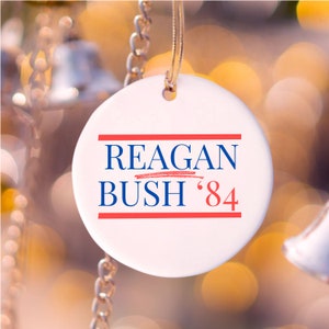 May include: White ceramic Christmas ornament with red and blue text that reads "REAGAN BUSH '84".