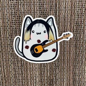 May include: A gray and white cartoon cat with long blonde hair playing a black bass guitar with a yellow pickguard. The cat is wearing a black shirt and has red roses on its body.