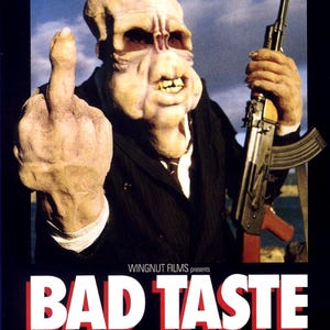 May include: Movie poster for the film "Bad Taste" featuring a grotesque alien-like creature giving the middle finger and holding a rifle. The poster is black with white and red text.