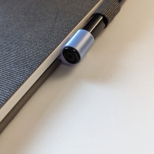 May include: A black pen with a gray pen holder attached to a gray notebook.
