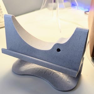 May include: A light gray 3D printed stand with the word "Supernote" printed on the base. The stand is designed to hold a tablet or e-reader.