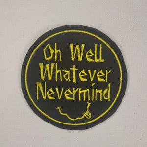 May include: Black and yellow embroidered patch with the text "Oh Well Whatever Nevermind" and a yellow smiley face.
