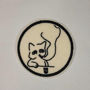 May include: A round, off-white patch with a black border. The patch features a black line drawing of a cat smoking a cigarette. The cat is holding a small glass. The design is centered within the patch.