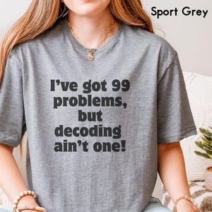 Puede incluir: Camiseta gris Sport con el texto negro "I've got 99 problems, but decoding ain't one!". La camiseta de manga corta es de color gris claro y está hecha de un material suave.