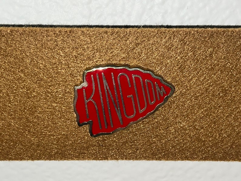 May include: A red and silver pin shaped like an arrowhead with the word "KINGDOM" written inside.