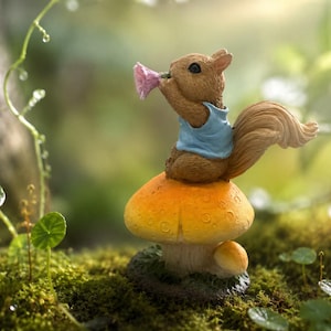 May include: A brown squirrel figurine wearing a light blue shirt, sitting atop a large orange and yellow mushroom. The squirrel is holding a small pink flower to its nose. The base of the mushroom is textured and sits on a mossy green surface.