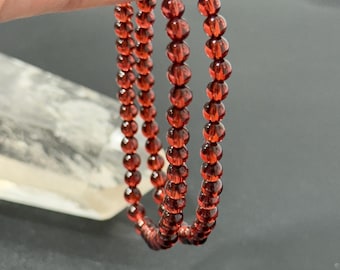 May include: Three strands of red beaded bracelets. Each bracelet is made of small, round, translucent beads. The bracelets are held up against a neutral background. The beads have a deep red color.