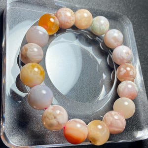 Puede incluir: Un brazalete hecho de cuentas redondas de ágata multicolores. Las cuentas son una mezcla de rosa, naranja y blanco.