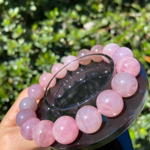 May include: A pink rose quartz bracelet with round beads. The bracelet is on a black display stand.