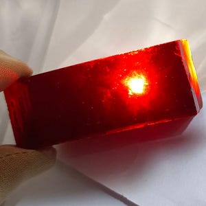 Puede incluir: Un bloque rectangular de vidrio translúcido de color rojo oscuro con una luz que lo atraviesa.