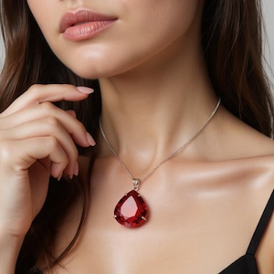 May include: A silver necklace featuring a large, teardrop-shaped, faceted red gemstone pendant. The pendant is suspended from a delicate silver chain. The gemstone has a vibrant, deep red color and is set in a silver bezel.