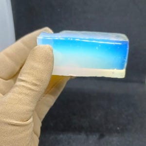 May include: A clear, rectangular block of resin with a blue and white layered design. The resin is translucent and has a slight iridescent sheen.