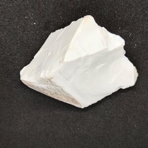 May include: A roughly shaped, off-white rock formation with a textured surface. The rock has a jagged edge and a light brown base, set against a dark background. The overall shape is irregular and natural.