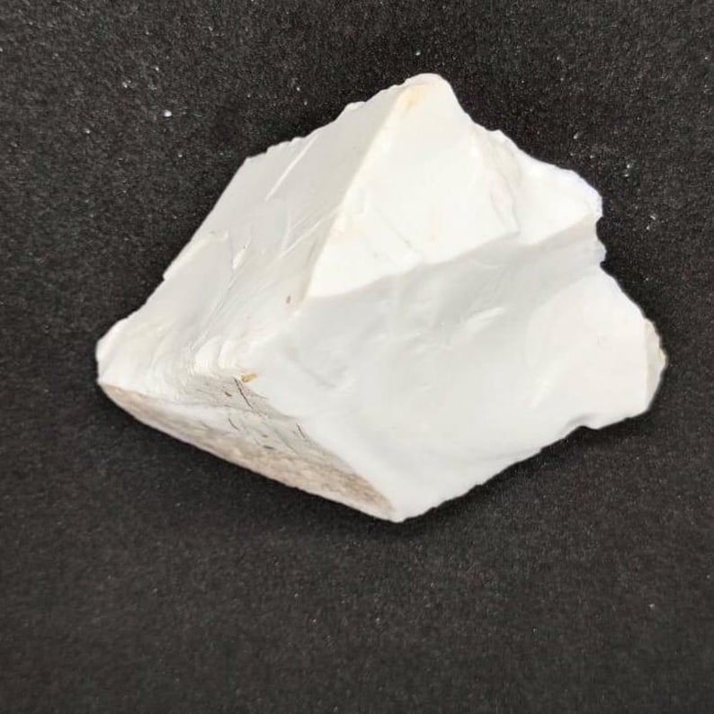 May include: A roughly shaped, off-white rock formation with a textured surface. The rock has a jagged edge and a light brown base, set against a dark background. The overall shape is irregular and natural.