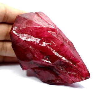 Peut inclure: Une grosse pierre précieuse de rubis rouge brute avec une pointe pointue. Le rubis a une couleur rouge foncé et riche et est translucide.