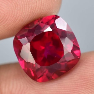 Può includere: Una pietra preziosa di colore rosso intenso con taglio a cuscino. La pietra preziosa è sfaccettata e ha un'alta lucidatura.