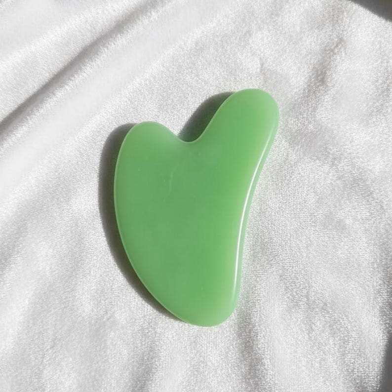 Natural green jade gua sha massage tool on white fabric