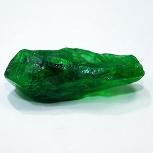 Puede incluir: Un gran cristal verde facetado con una textura rugosa y natural. El cristal es translúcido y tiene un ligero brillo.